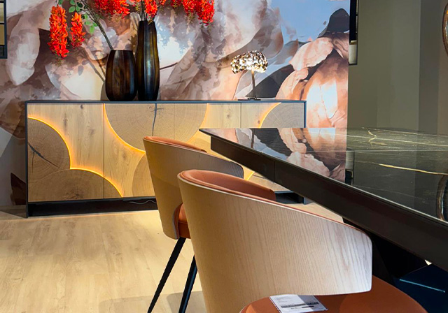 Salle à manger contemporaine avec buffet design en bois sculpté et rétroéclairé, chaises en bois clair et assise cuir, table noire brillante.